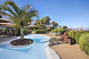 A pool area with palm trees, a rock formation, and outdoor seating.