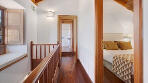 A narrow hallway with wooden railings, a bed with patterned bedding, and a visible bathroom in the background.