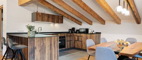 Una cocina moderna con vigas de madera, una isla central, taburetes de bar y una mesa de comedor con sillas.