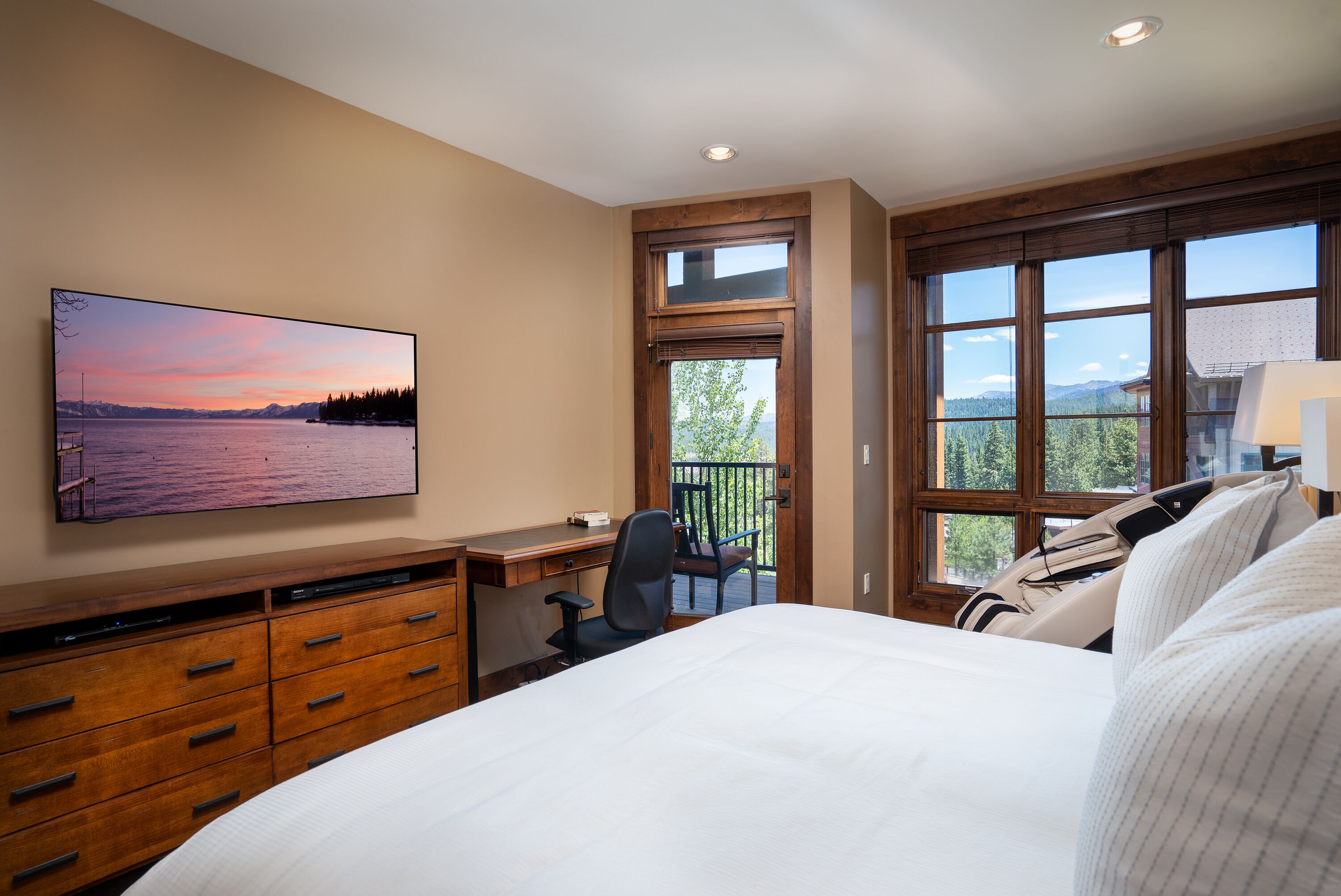 A bedroom with a bed, a desk, a chair, a TV, and a window with a view of the outdoors.
