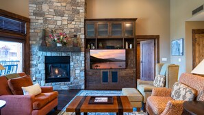 A cozy living room with a stone fireplace, comfortable seating, and a television. - Luxury 2BD Village at Northstar Residence w/ Ski Valet (Truckee)
