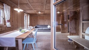 Een houten interieur met een eettafel, stoelen, een bank en een glazen deur.