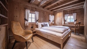 Een slaapkamer in een houten blokhut met een bed, een stoel en twee ramen.