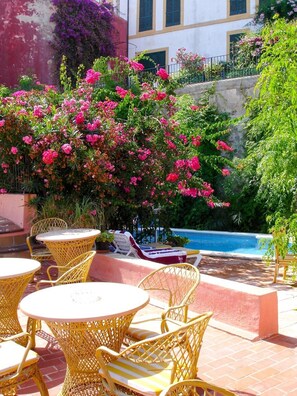 Terraza al aire libre con mesas y sillas, piscina y abundante vegetación.