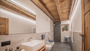 Ein modernes Badezimmer mit einem großen Spiegel, Holzbalkendecke, einem weißen Waschbecken, einer Toilette und einer Duschkabine.