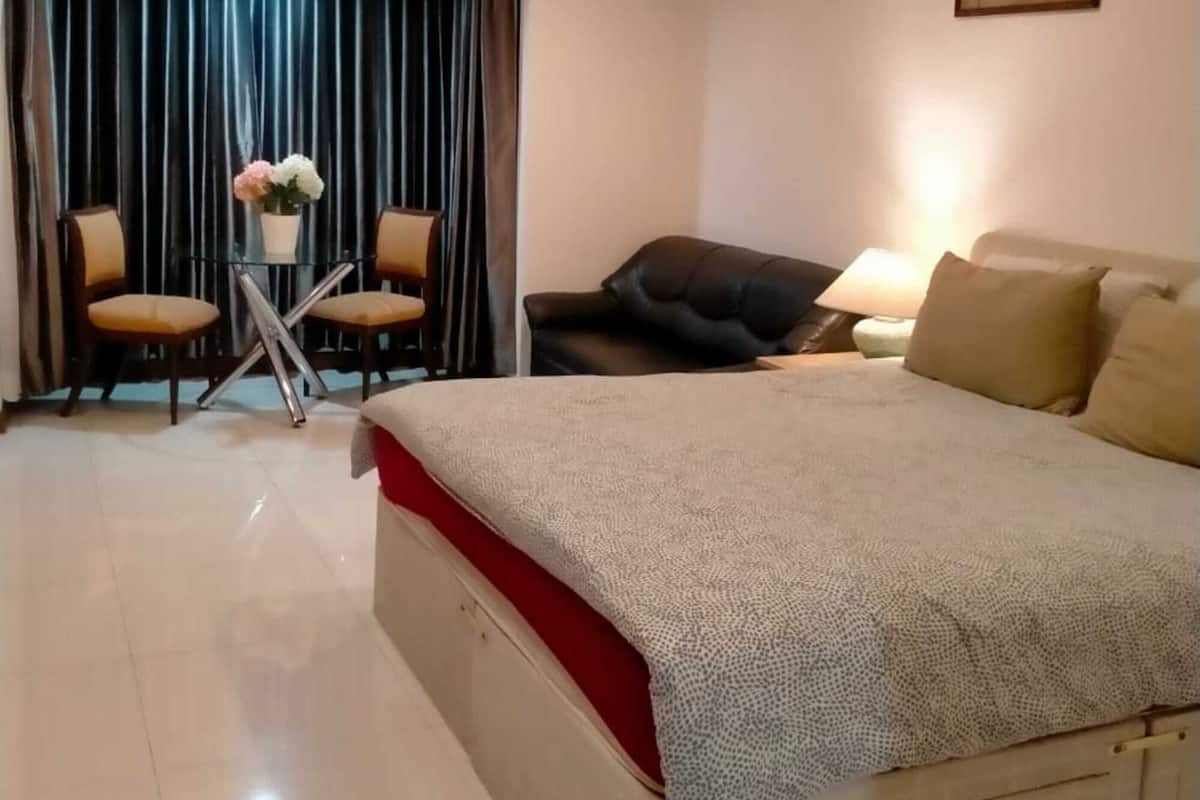 A hotel room with a large bed, a desk with two chairs, a sofa, and a painting on the wall.