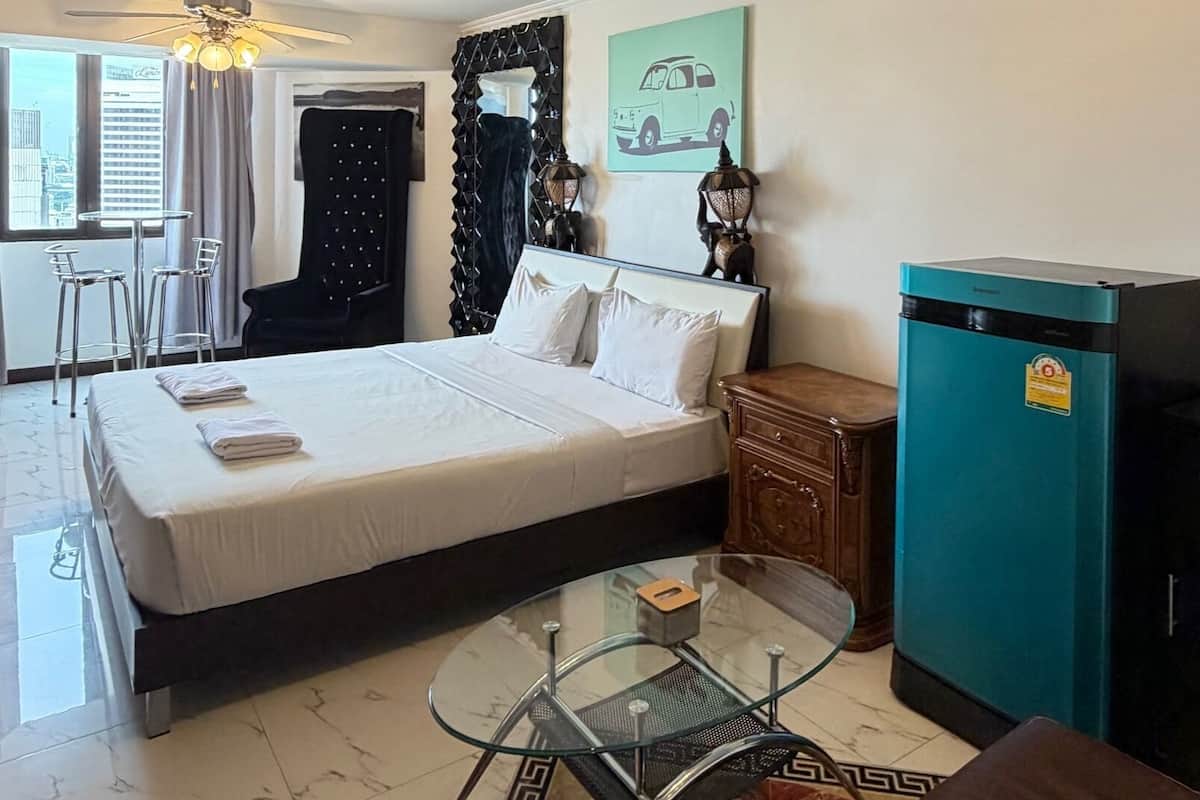 A hotel room with a bed, a glass coffee table, a sofa, a minibar, and a view of the city.