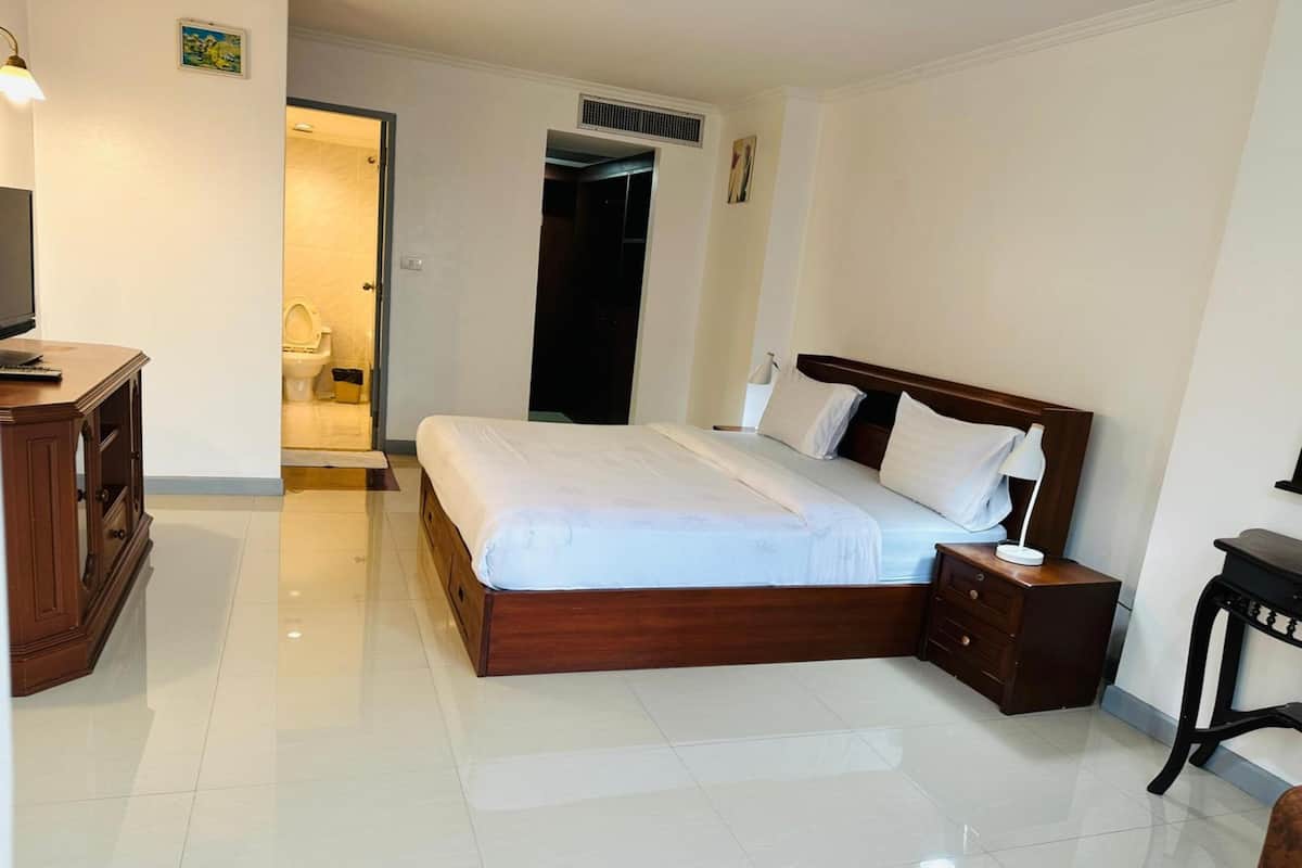 A hotel room with a wooden bed, a nightstand, a desk, and a chair.