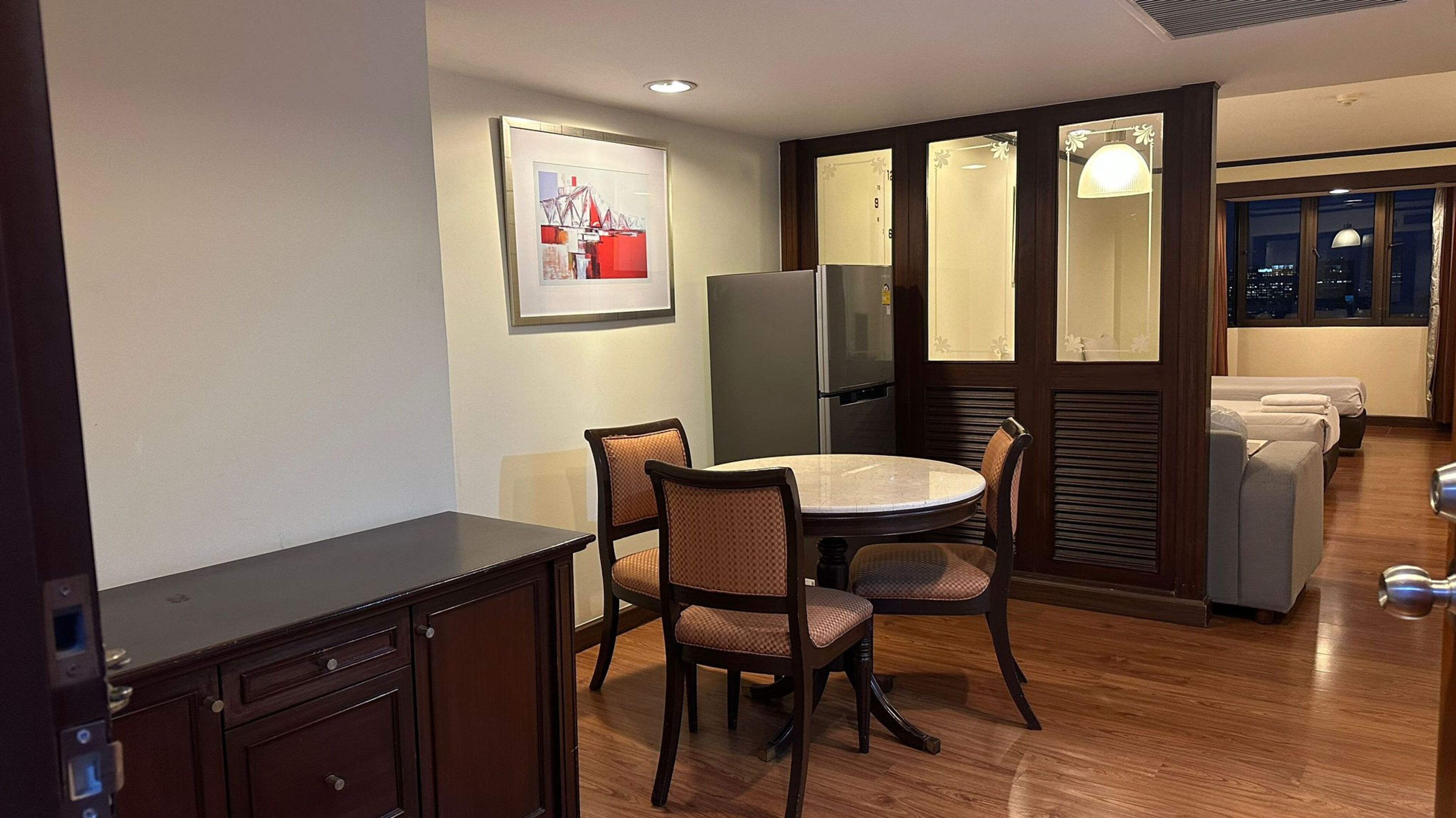 A compact hotel room with a dining area, a refrigerator, a bed, and a city view through the window.