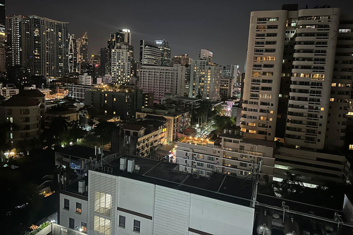 A nighttime cityscape with high-rise buildings, illuminated windows, and a mix of architectural styles.