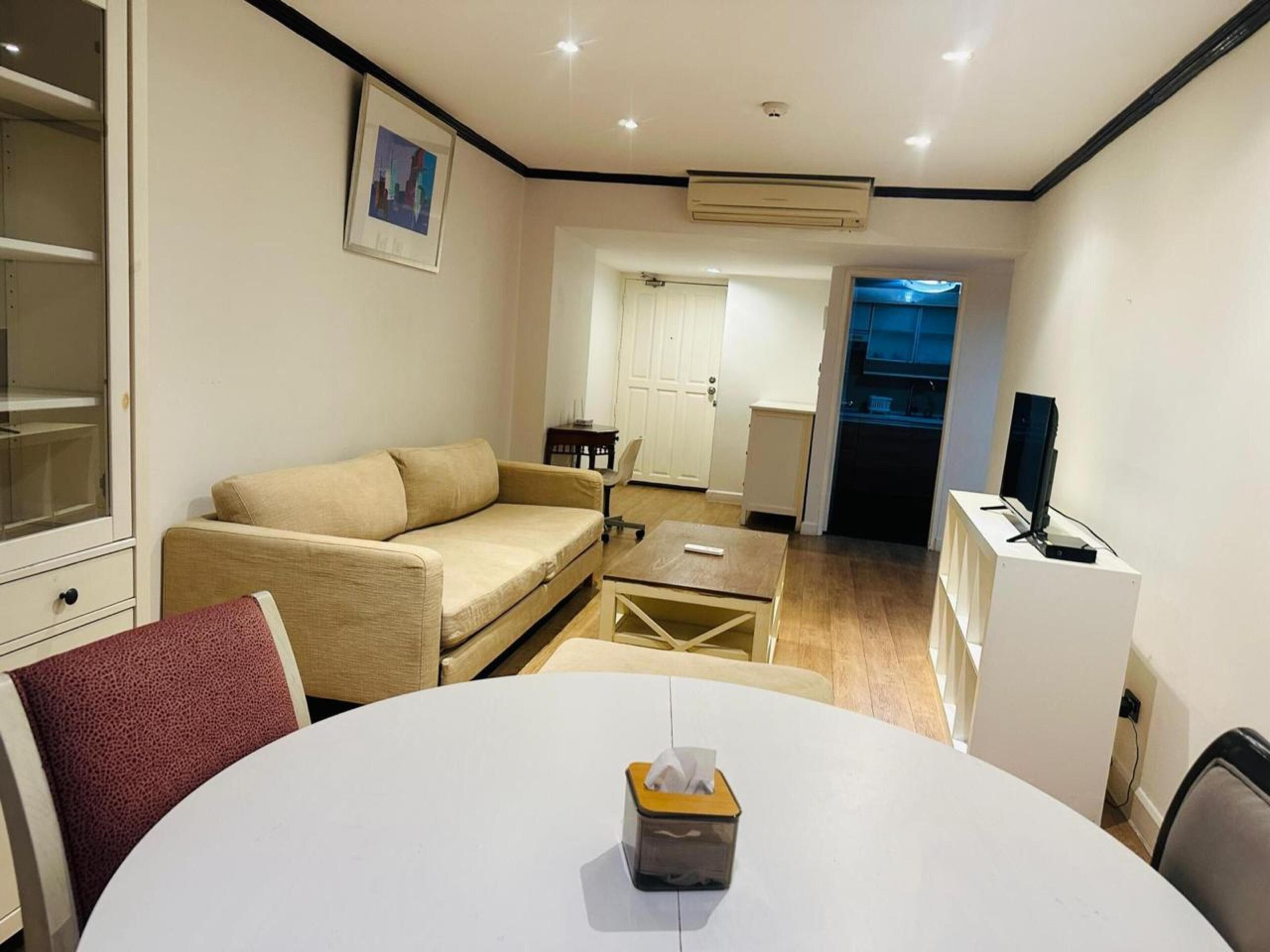 A compact living space with a sofa, a small dining table, a TV, and a kitchenette.
