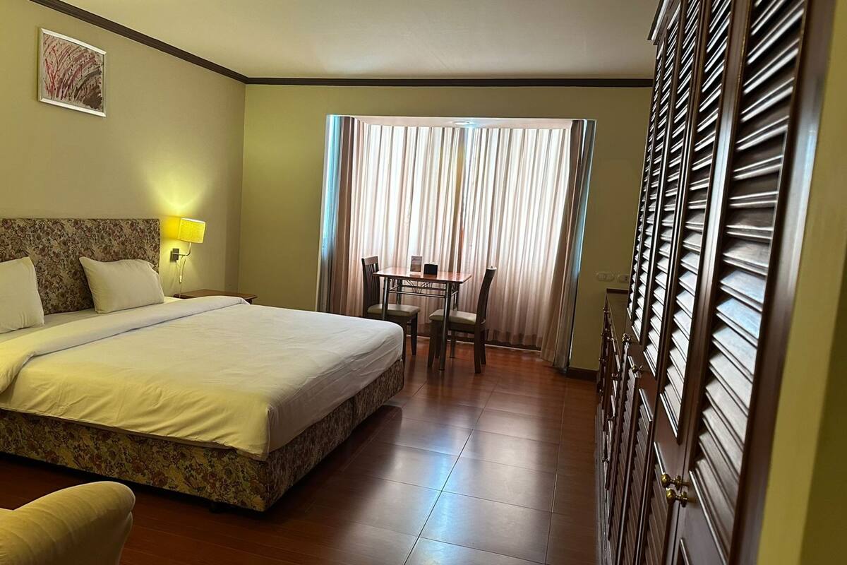 A hotel room with a large bed, a desk, a chair, and a window with curtains.