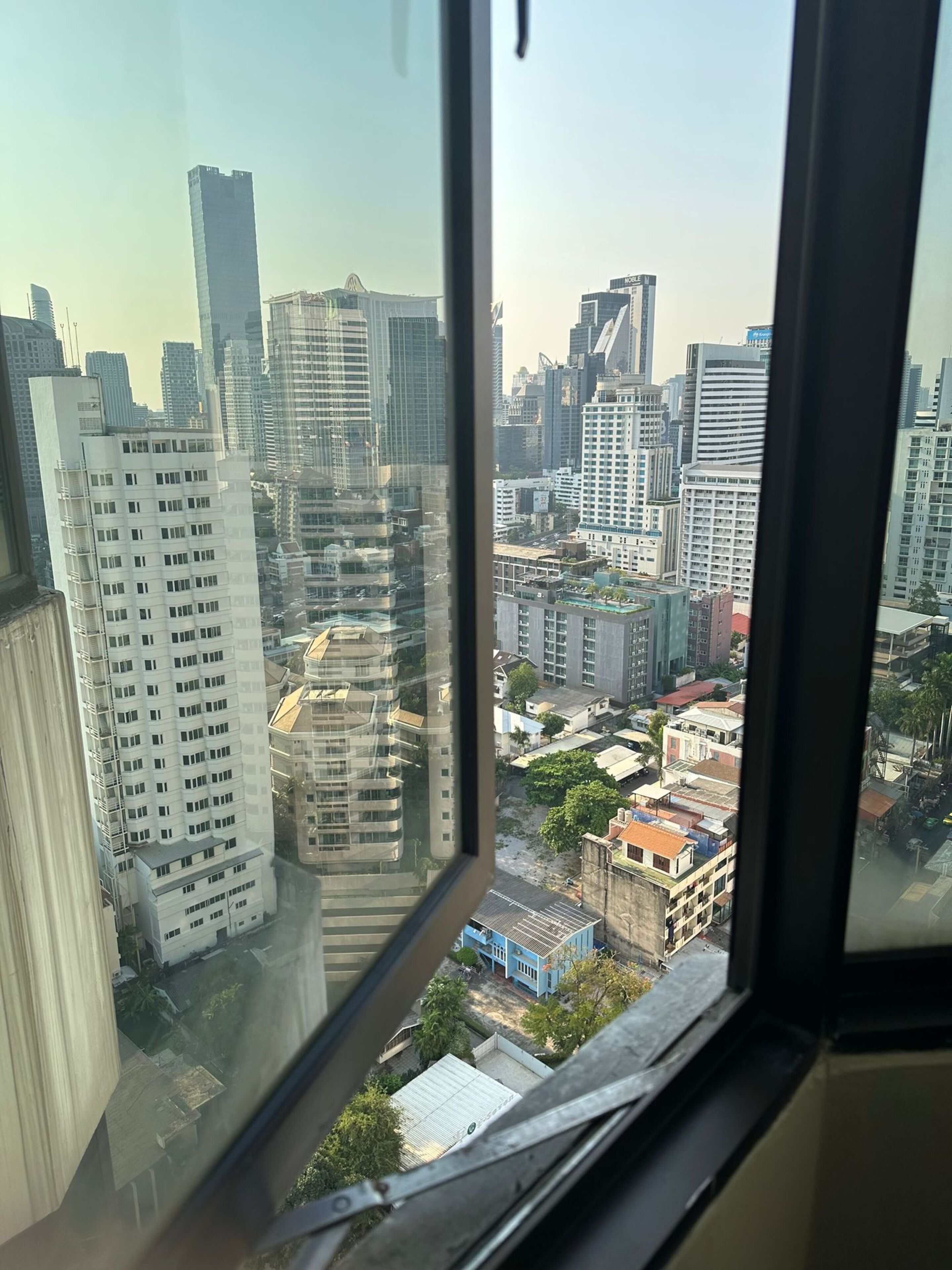 A view from a high-rise window overlooking a cityscape with various buildings, including high-rise and mid-rise structures.