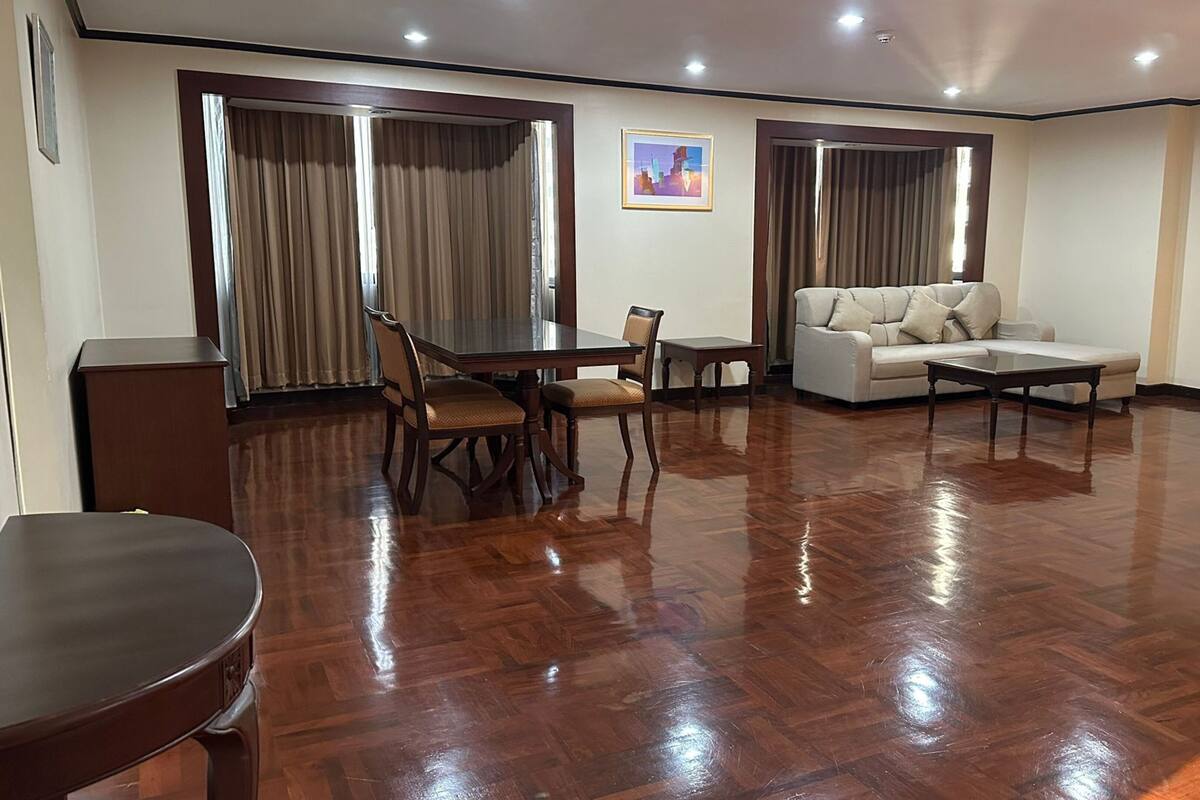 A spacious living room with a wooden floor, a dining table with chairs, a sofa, and a coffee table.