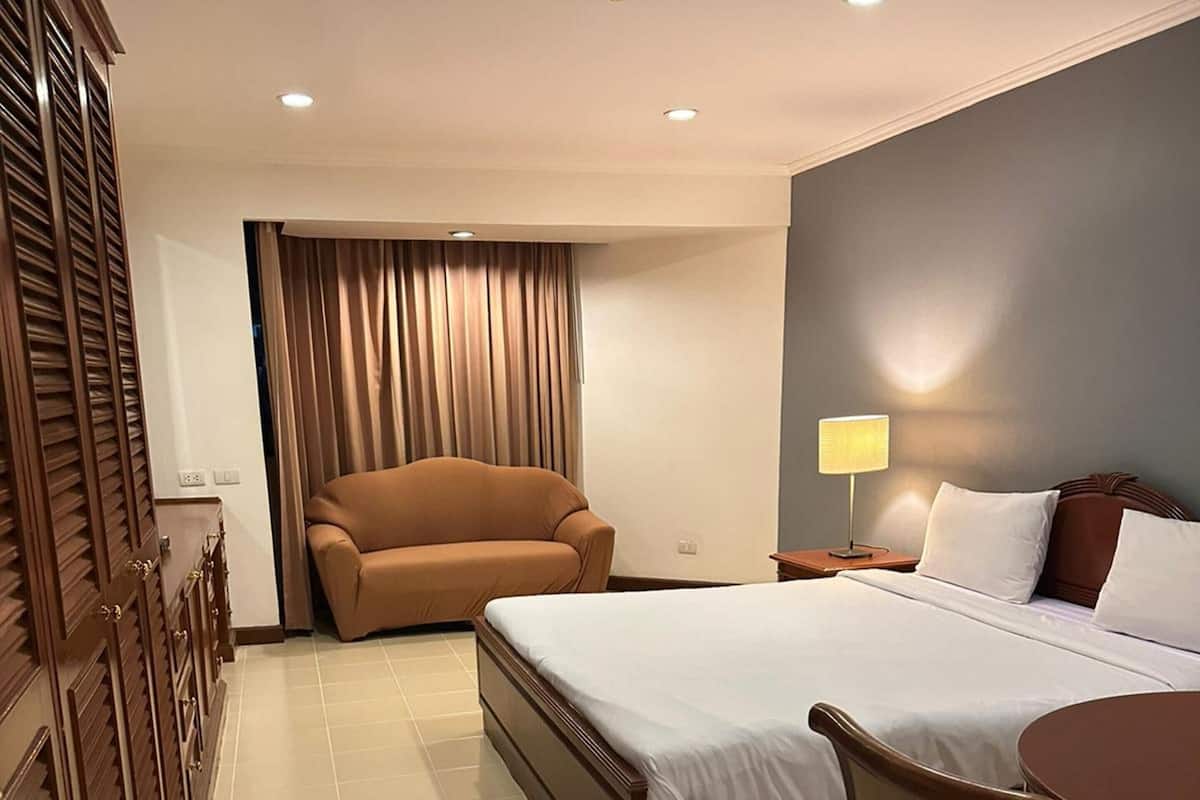 A hotel room with a bed, a chair, a desk, and a lamp.