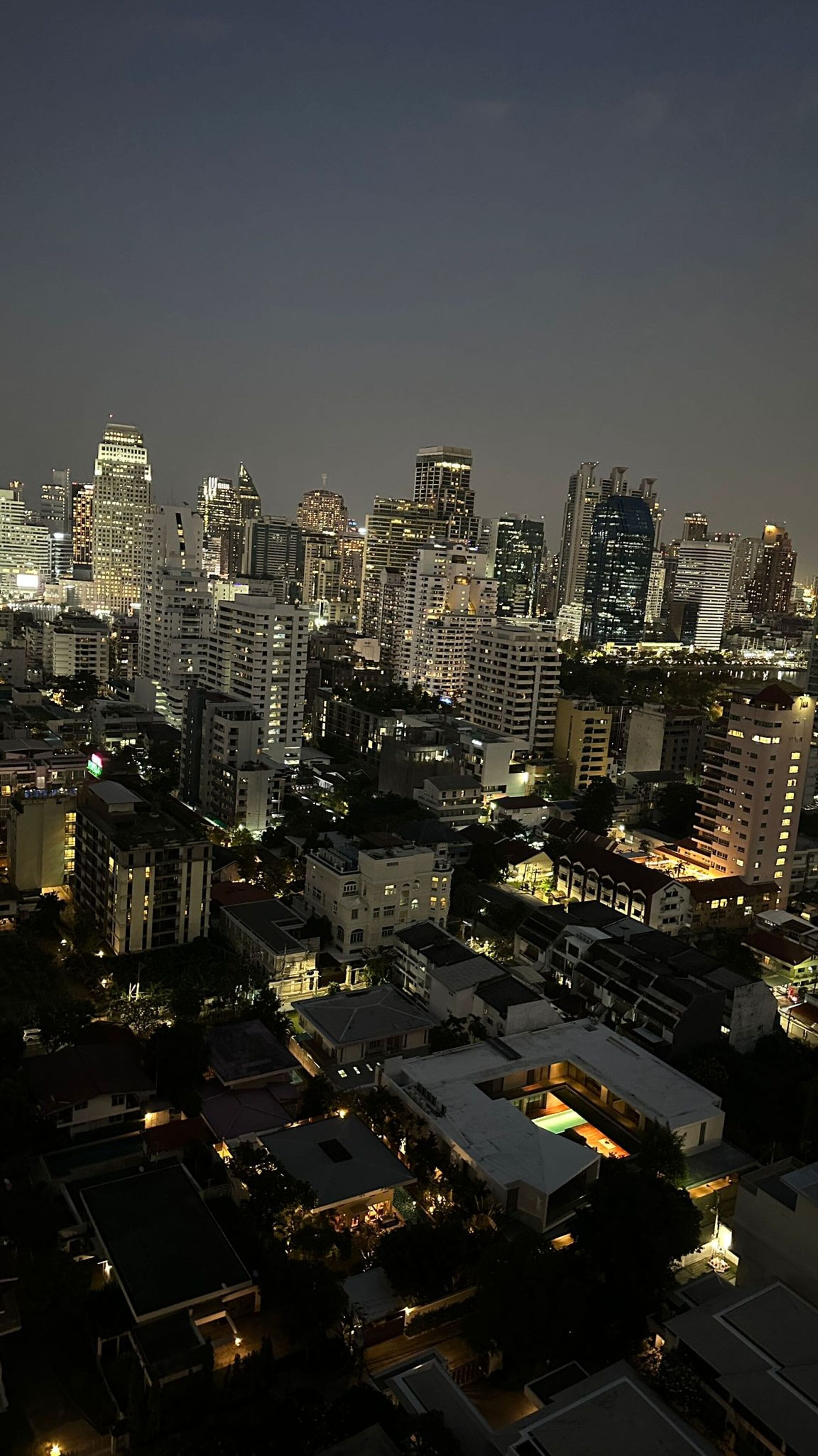 A nighttime cityscape with high-rise buildings, some with illuminated windows, and a mix of residential and commercial structures.