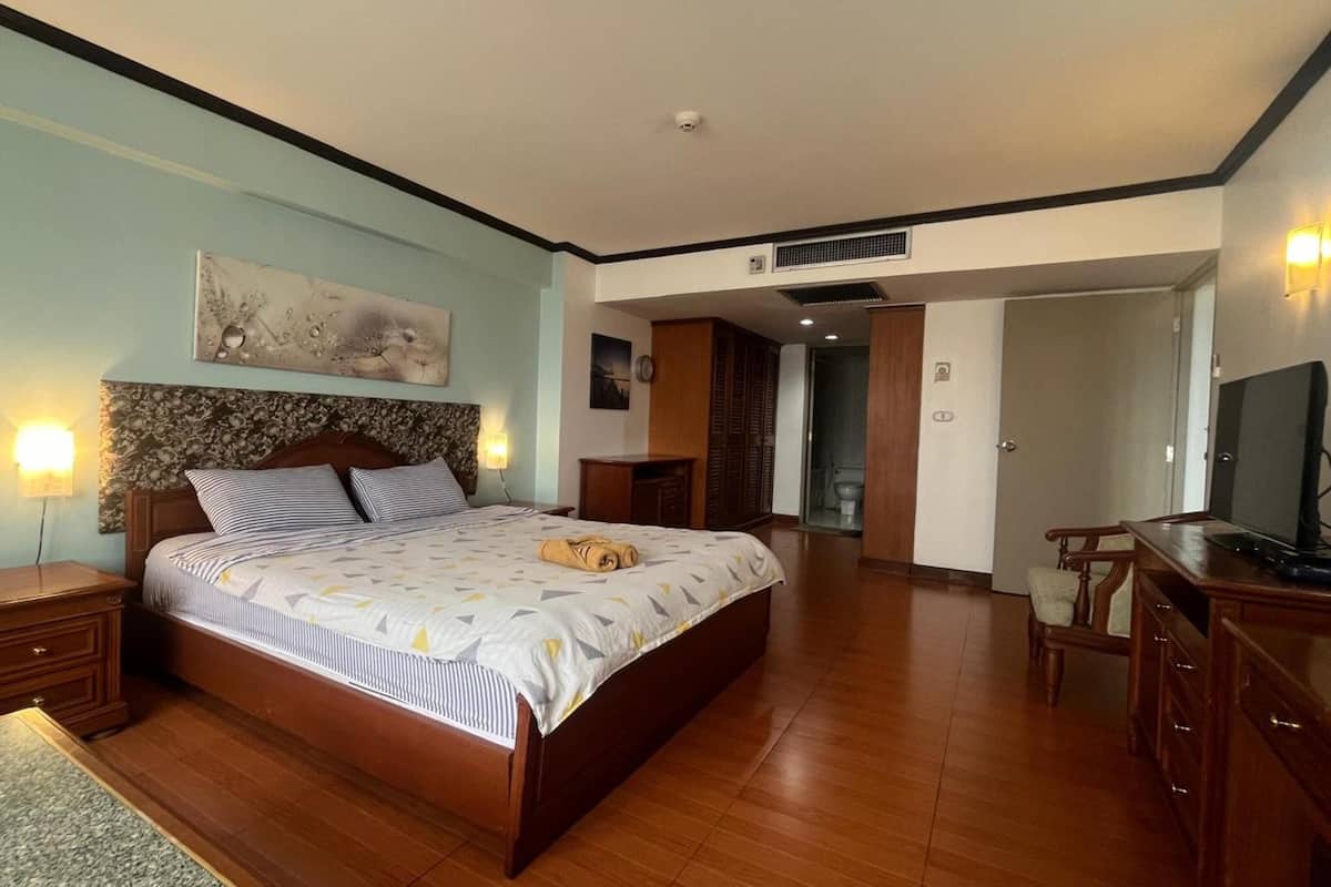 A bedroom with a large bed, wooden headboard, two bedside tables, a TV, and a wardrobe.
