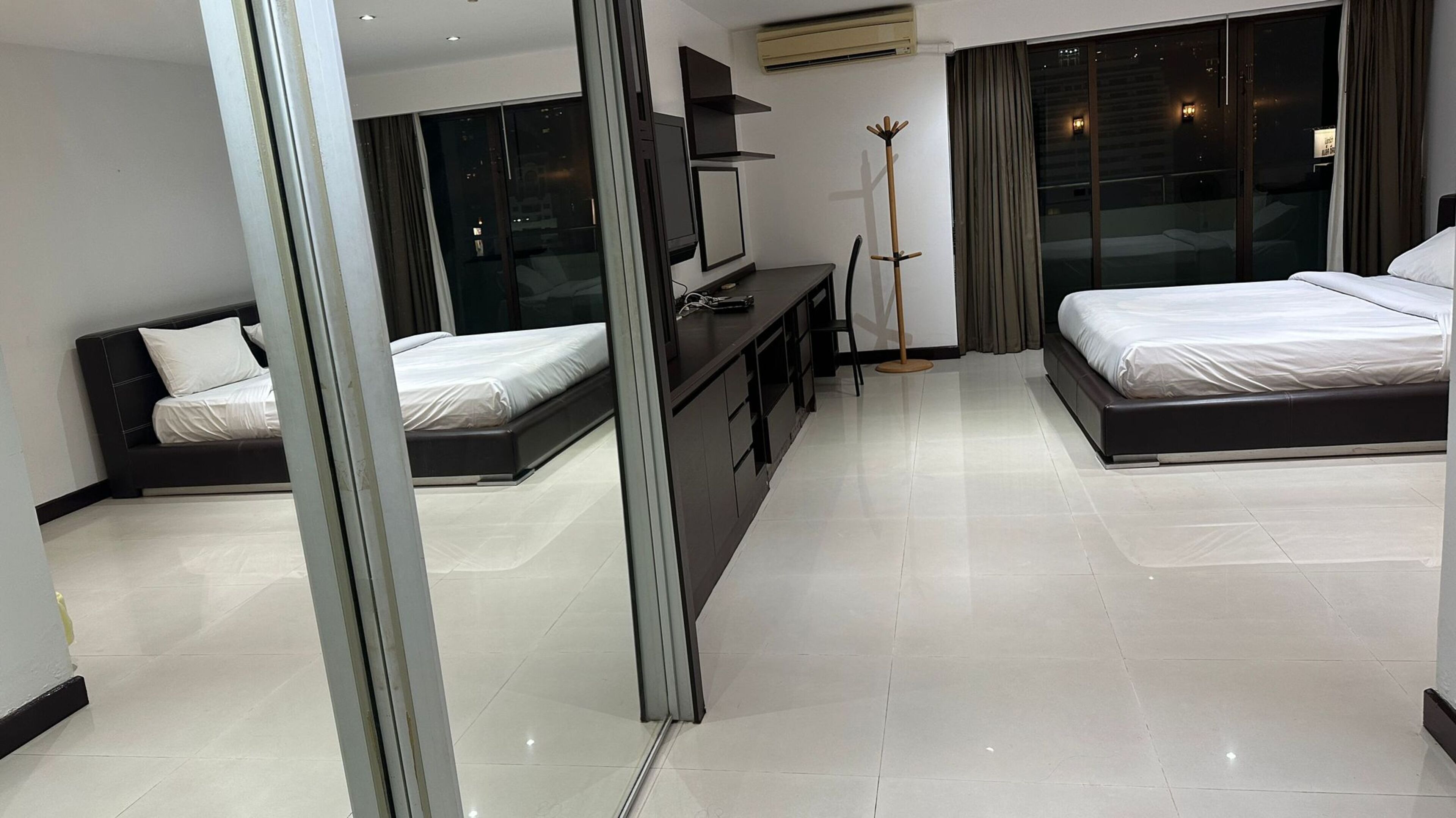 A modern hotel room with two beds, a desk, and a large window.