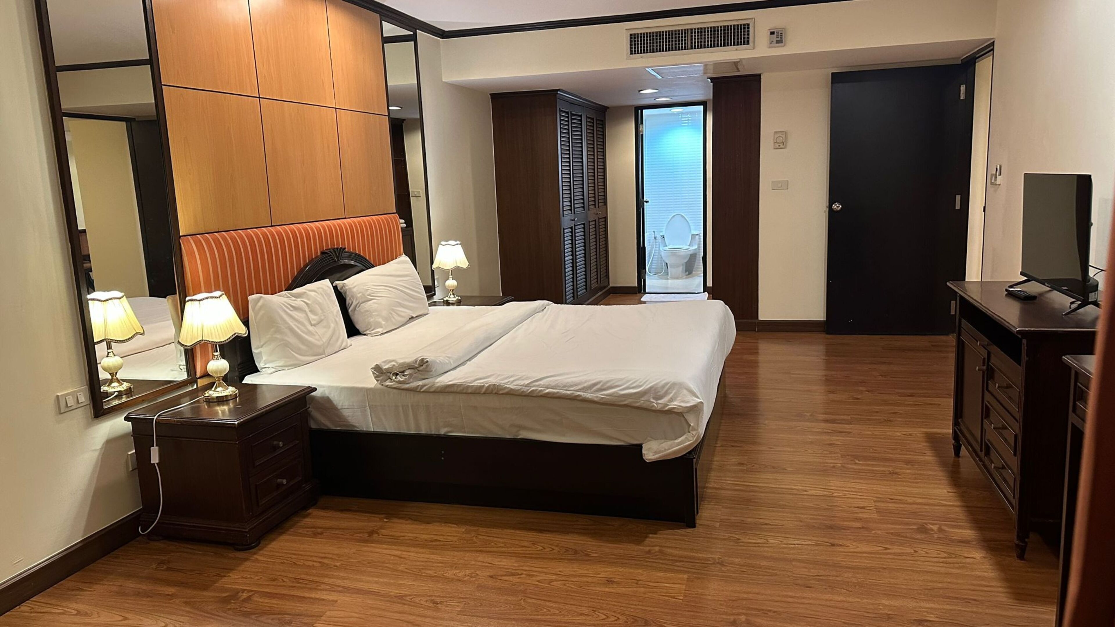 A hotel room with a large bed, a dresser, a mirror, and a television.
