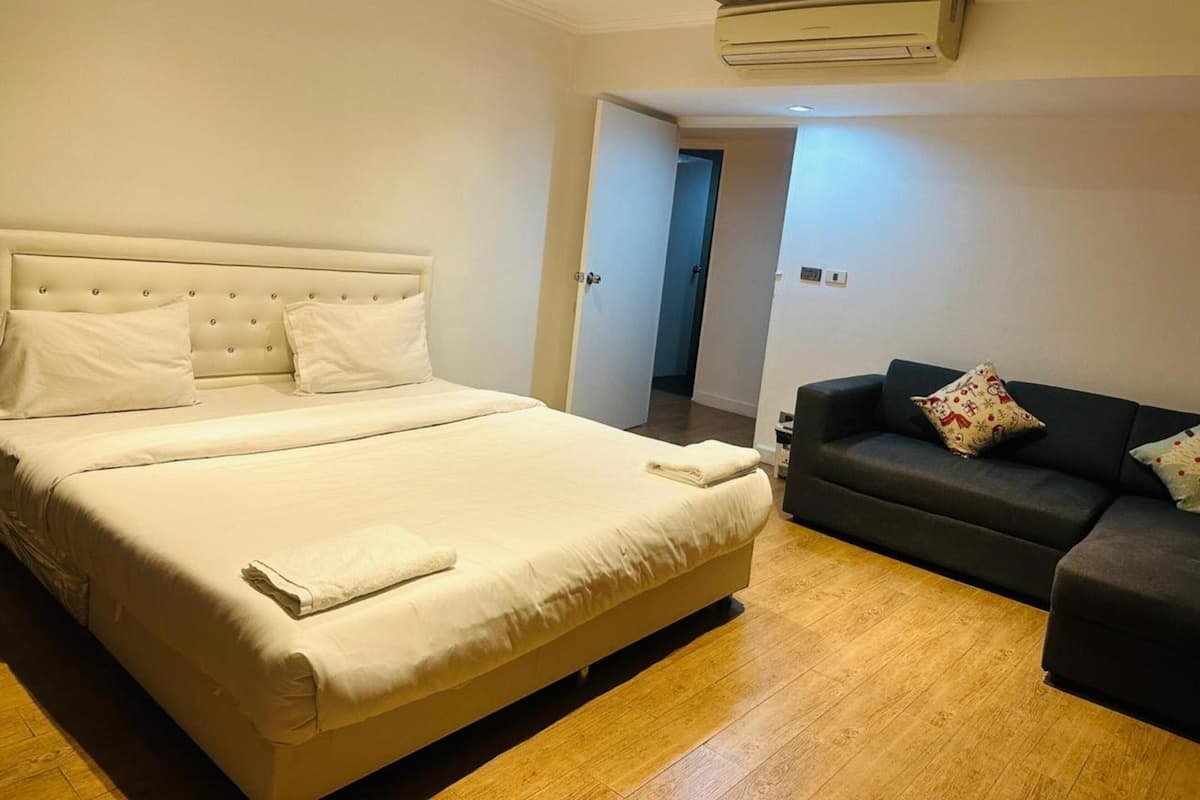 A bedroom with a large bed, a dark-colored sofa, and a wooden floor.