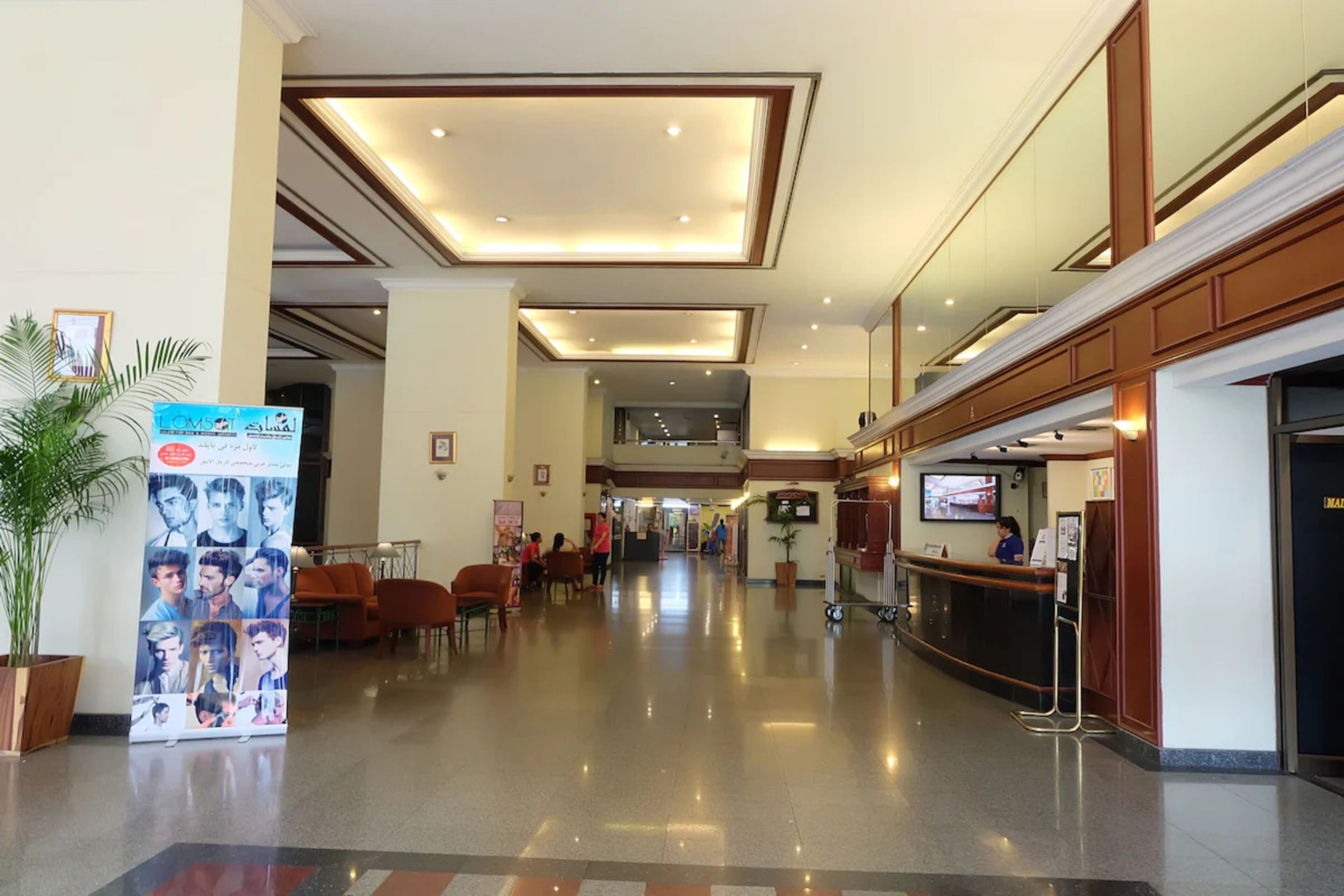 Un hall de hotel con mostrador de recepción, zona de estar y un cartel grande.