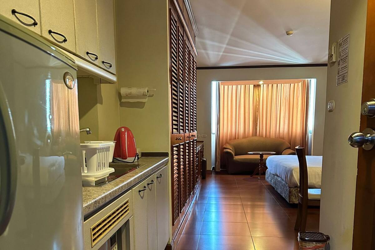 A hotel room with a kitchenette, a bed, a sofa, and a view of the outdoors.