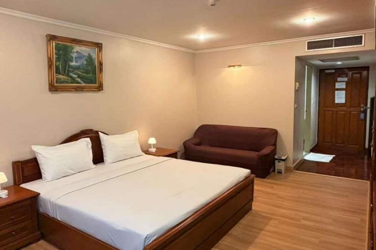 A bedroom with a wooden bed, a nightstand, a lamp, a painting on the wall, and a door leading to another room.