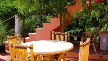 A round table with six chairs, surrounded by lush greenery and a staircase.