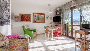 Ein Wohnzimmer mit Essbereich, einem grünen Sessel, einem roten Sessel, einem Fernseher und einem Fenster mit Vorhängen.