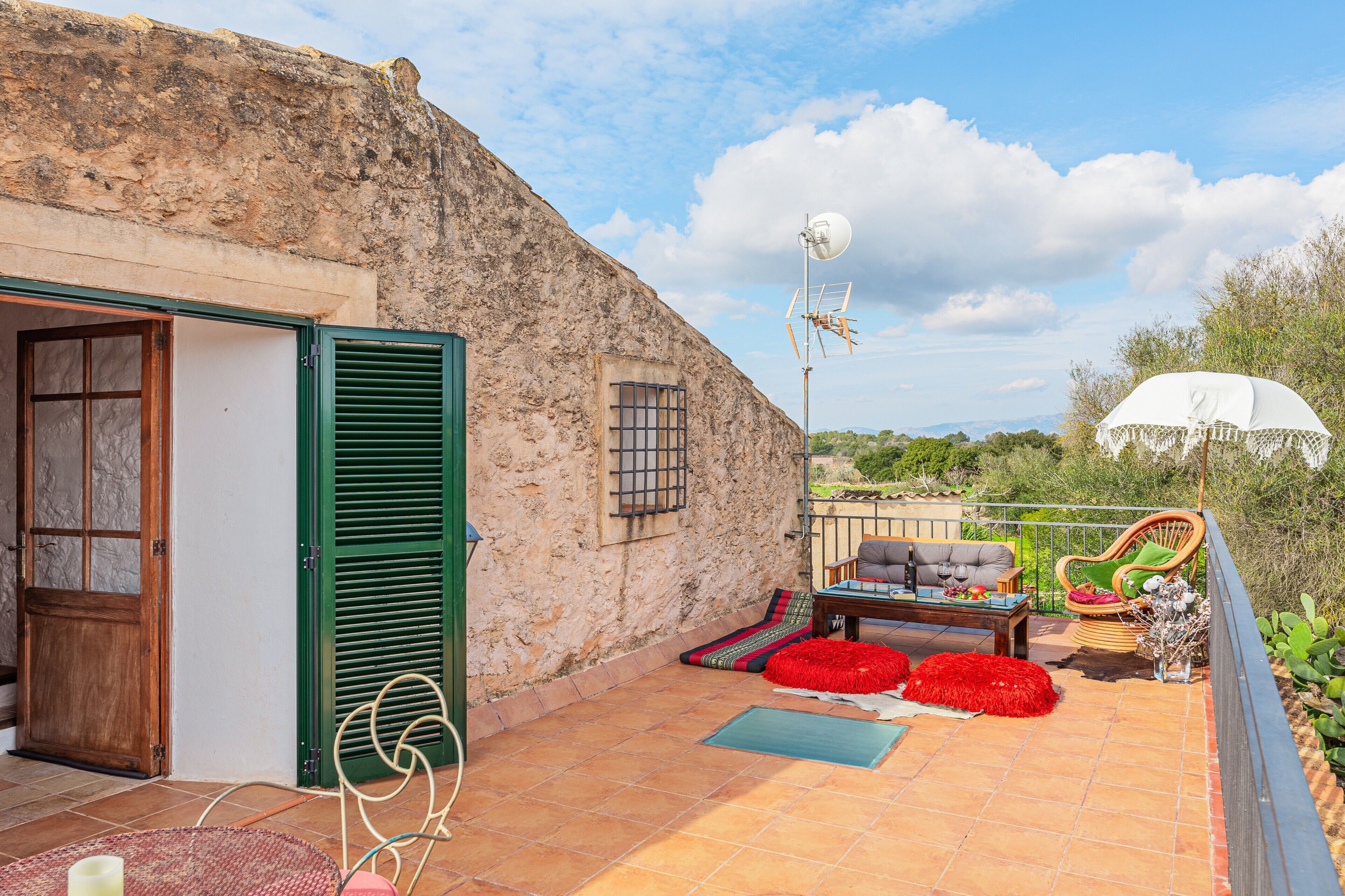 Un bâtiment rustique en pierre avec une porte verte, une terrasse dotée de mobilier d’extérieur et un parasol blanc.
