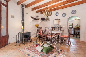 Un salon chaleureux avec une cheminée, des poutres apparentes, une table à manger avec des chaises et un tapis à motifs.