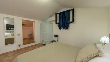 A bedroom with a bed, a wardrobe, a chair, a mirror, and a door leading to another room.