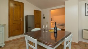 Un petit coin repas avec une table en bois, deux chaises blanches, un réfrigérateur et une bouteille de vin.