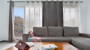 Una sala de estar con un sofá, una mesa de centro y un ventanal con cortinas.
