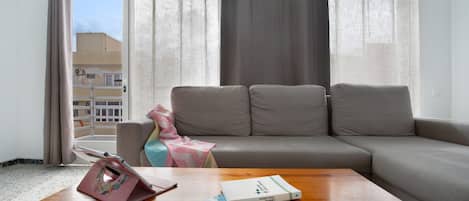 Una sala de estar con un sofá, una mesa de centro y un ventanal con cortinas.