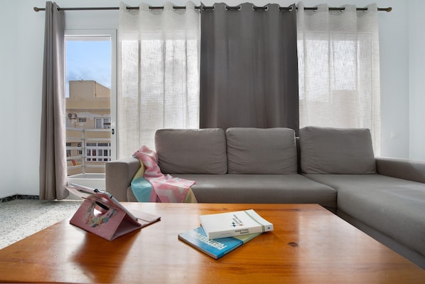 A living room with a sofa, a coffee table, and a window with curtains.