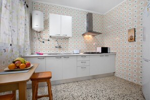 Una cucina con mobili bianchi, uno scaldabagno, un forno a microonde e una ciotola di frutta sul piano di lavoro.