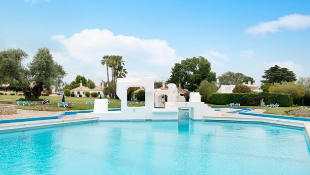 A swimming pool with white structures, surrounded by greenery and trees. - Holiday Home 'Pedras Del Rei Ll' with Shared Pool, Wi-Fi and Air Conditioning (Tavira)
