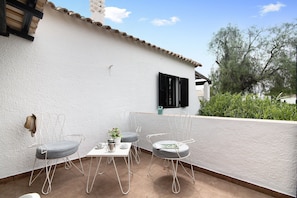 Une terrasse avec deux chaises en métal, une table et un pot de fleurs.