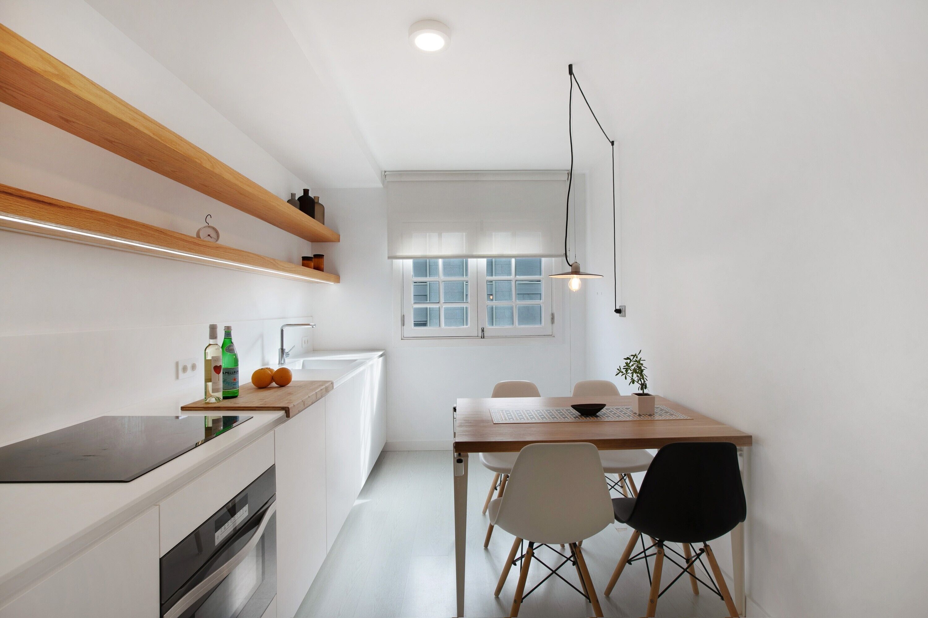 A modern kitchen with wooden shelves, a dining table with chairs, and a pendant light.
