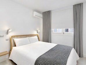 Une chambre à coucher moderne avec un cadre de lit en bois, une literie blanche, un plaid tricoté gris et une fenêtre avec des rideaux.