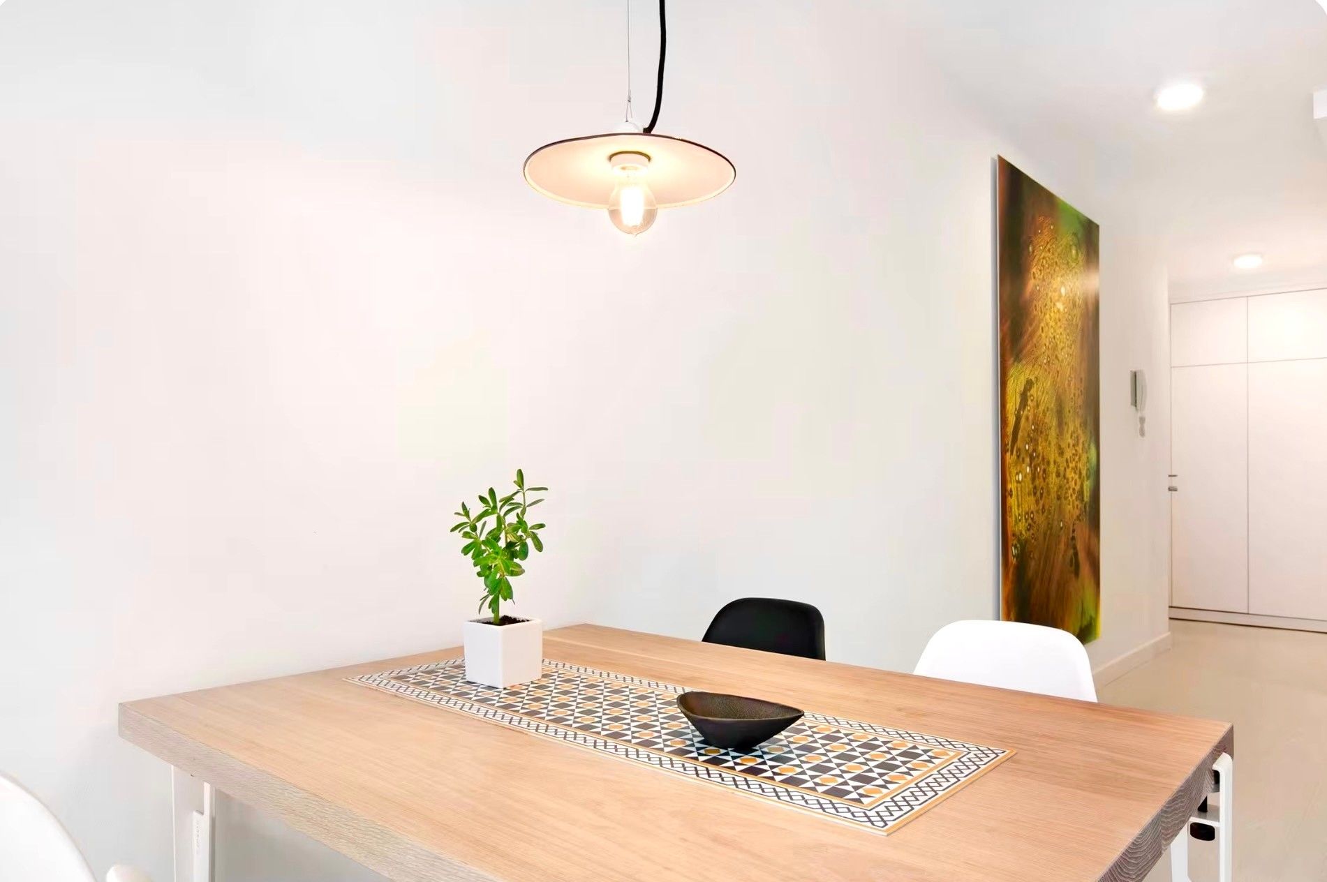 A modern dining area with a wooden table, a potted plant, and a decorative bowl.
