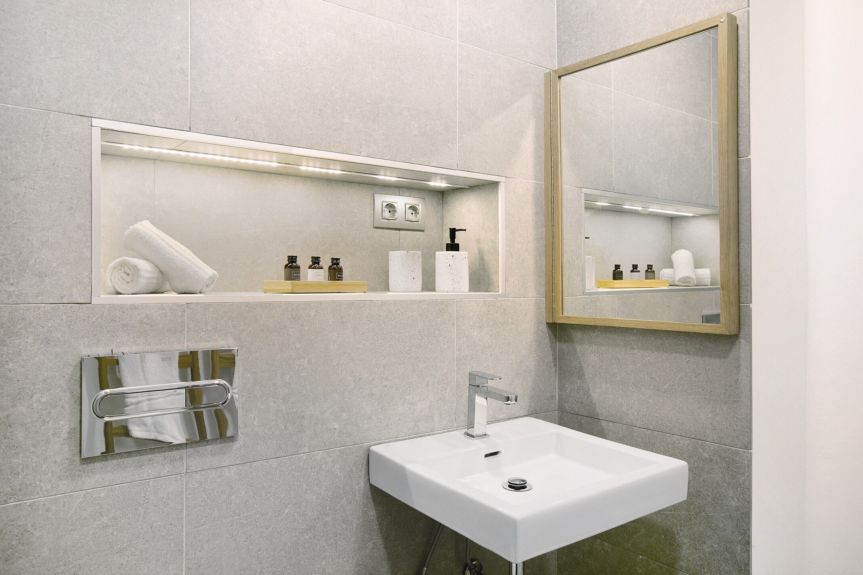 A modern bathroom with a white sink, a towel rack, a mirror, and shelves with toiletries.