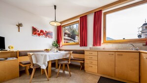 Een keuken met houten kastjes, een eettafel met stoelen, een raam met rode gordijnen en uitzicht op een gebouw.
