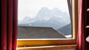 Uitzicht vanuit een raam op een bergketen, met het dak van een gebouw en een houten raamkozijn.