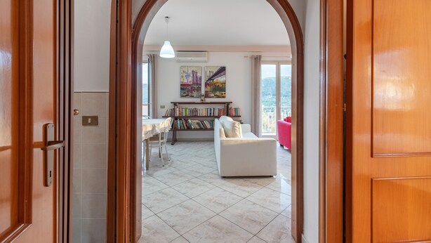 Ein offenes Durchgang zu einem Wohnzimmer mit weißem Sofa, einem Esstisch und einem Bücherregal.