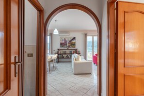 Ein offenes Durchgang zu einem Wohnzimmer mit weißem Sofa, einem Esstisch und einem Bücherregal.