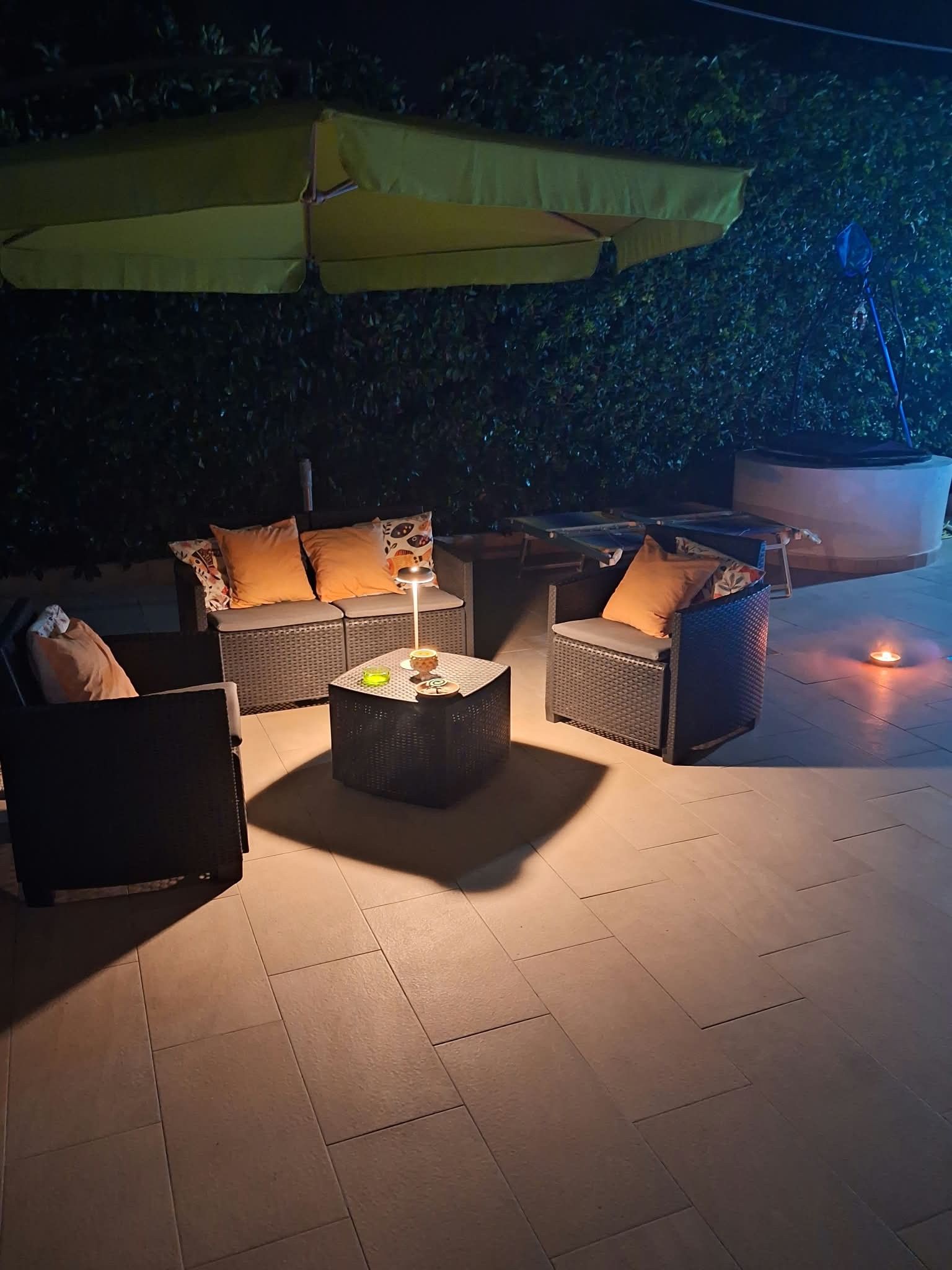 Un espace extérieur aménagé avec une table ronde, deux canapés et un fauteuil, le tout installé sous un parasol jaune.