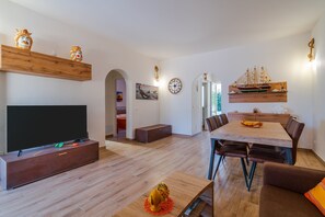 Un salon moderne doté d’un téléviseur à écran plat, de meubles en bois, d’un coin repas avec une table et des chaises en bois, et d’objets décoratifs disposés sur des étagères.