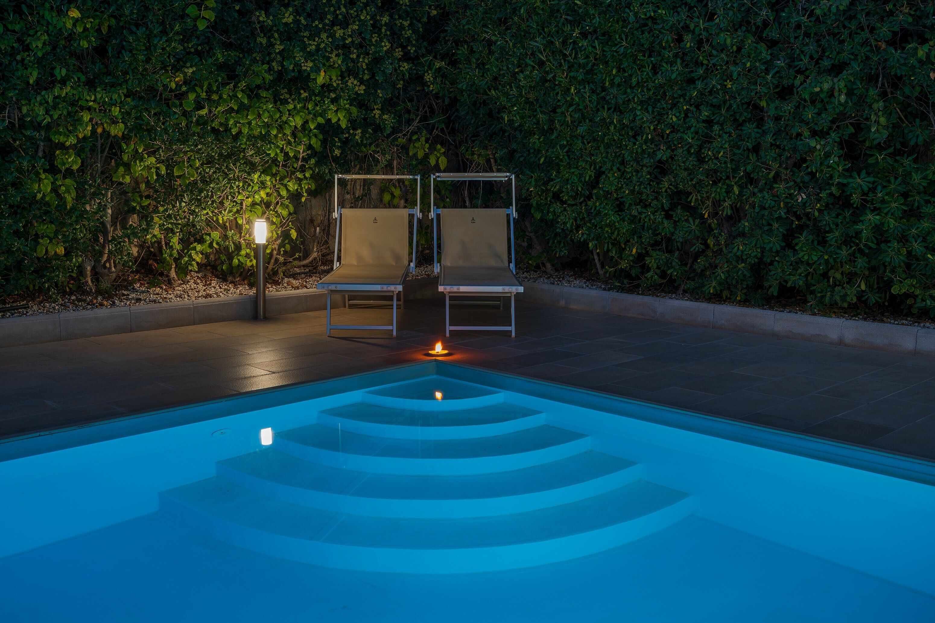 A swimming pool with a geometric design, two lounge chairs, and a wall-mounted light.
